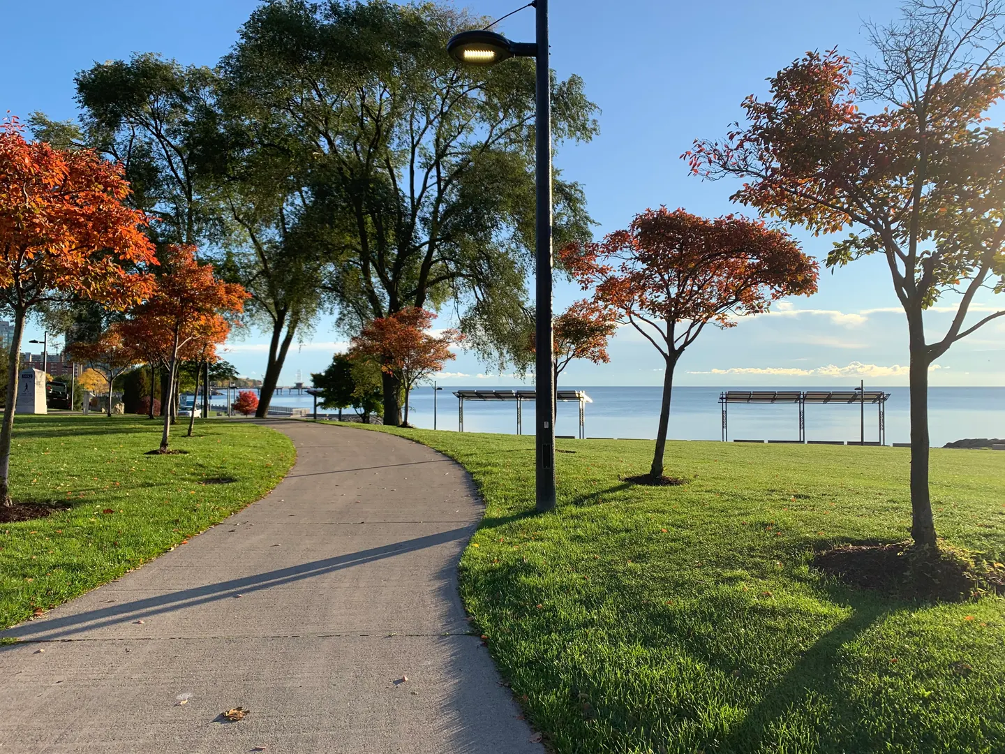 Paved path curving through Spencer Smith Park with orange autumn trees and Lake Ontario beyond
