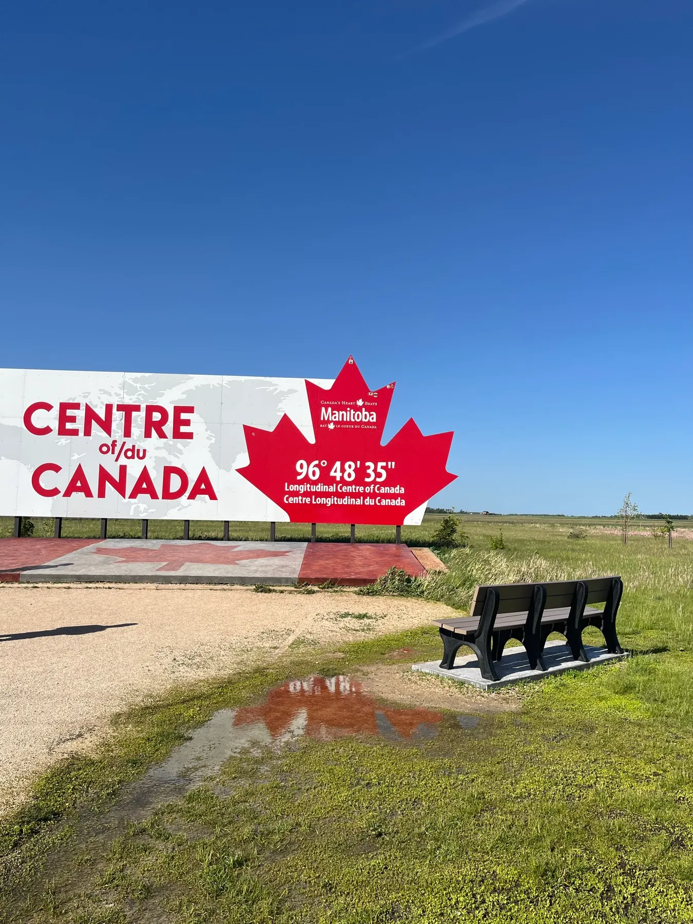 The longitudinal Centre of Canada sign beneath a wide prairie sky
