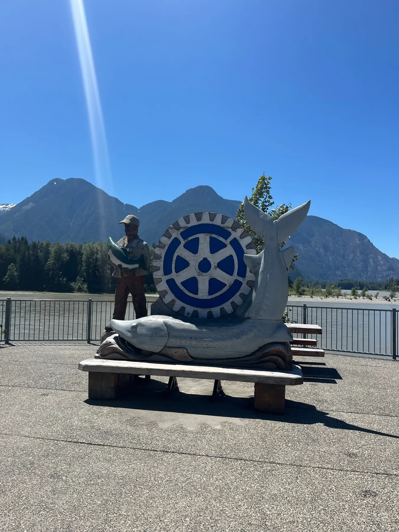 A fisherman and stylized fish carving beside the river in Hope