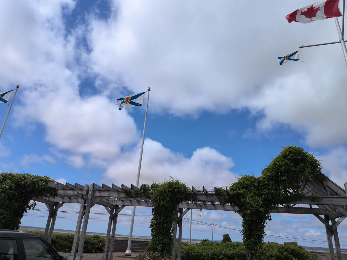 Canadian and Nova Scotia flags flying above a vine-covered pergola at the visitor centre
